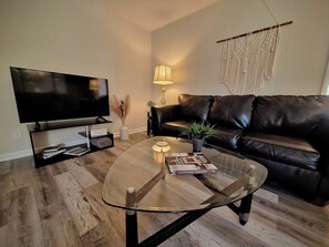 Ein modernes Wohnzimmer mit Glastisch, schwarzem Ledersofa, Flachbildfernseher, Lampe und Wandbild.