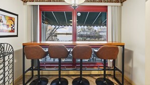 Eine Bar mit drei Hockstühlen, einem Fenster mit rotem Rahmen und einer Pendelleuchte.