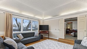 Ein modernes Wohnzimmer mit grauem Sofa, einem Flachbildfernseher und einem großen Fenster.
