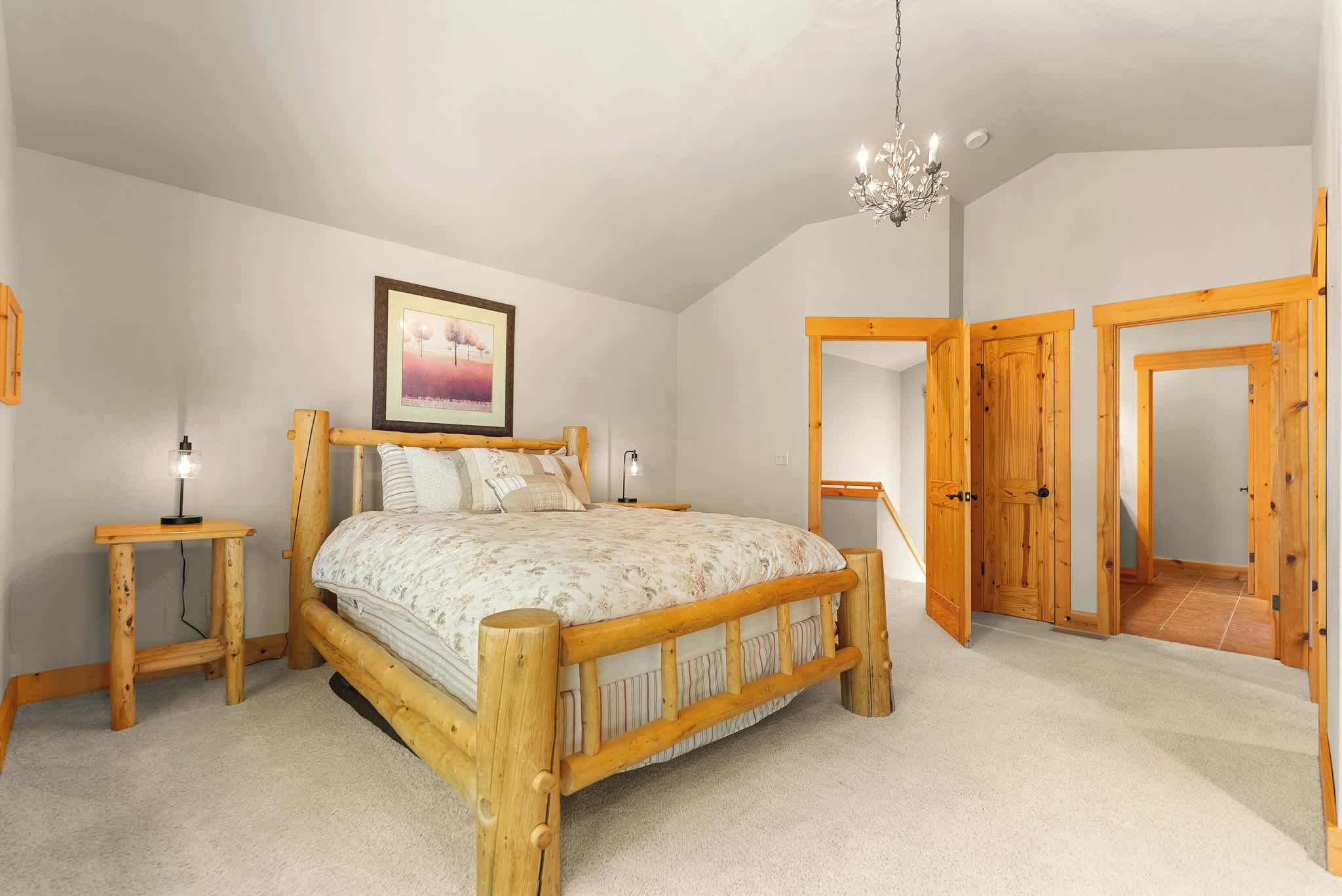 Une chambre à coucher avec un lit en bois, une table de chevet, un lustre et un tableau encadré au mur.