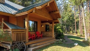 Eine Holzhütte mit Veranda, roten Stühlen und einem Holzwagen.