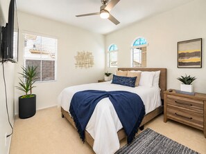 Ein Schlafzimmer mit einem Bett, Nachttischen, einem Deckenventilator, einer Topfpflanze und einem an der Wand befestigten Fernseher.