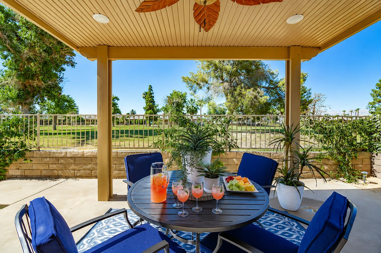 A covered patio with a table set for two, featuring a fruit platter and drinks.
