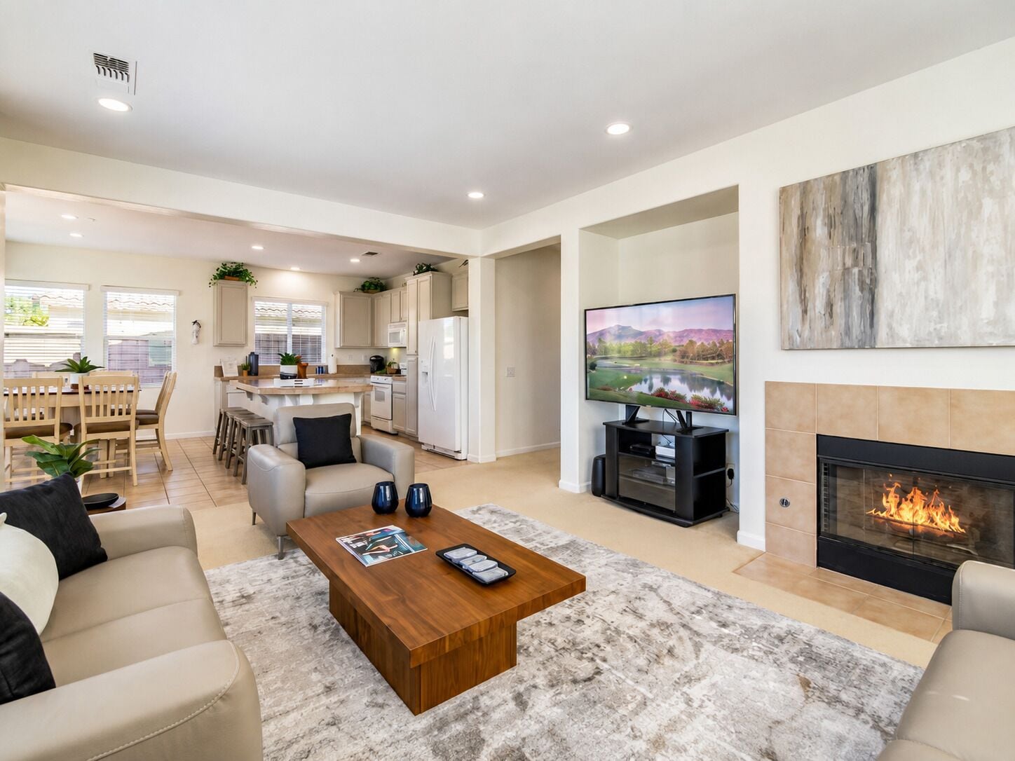 A modern living room with a fireplace, a television, and a kitchen in the background.