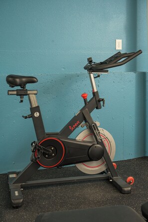 Ein Ergometer mit schwarzem Sattel und Lenker, vor einer türkisfarbenen Wand platziert.