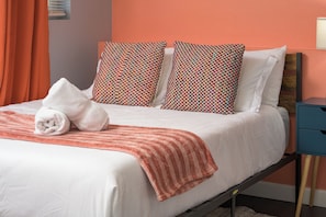 A neatly made bed with a striped blanket, two patterned pillows, and a rolled towel.