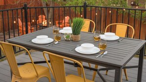 Un espace extérieur aménagé pour les repas, avec une table dressée pour quatre personnes, entourée de chaises jaunes, et une clôture en bois en arrière-plan.