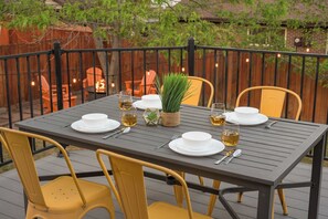 An outdoor dining area with a table set for four, surrounded by yellow chairs, and a wooden fence in the background.