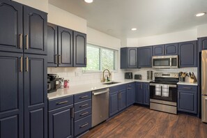 A modern kitchen with dark blue cabinets, stainless steel appliances, and a wooden floor.