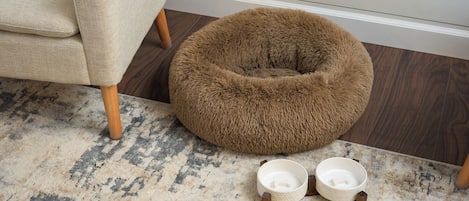 A pet bed and two pet bowls on a patterned rug.
