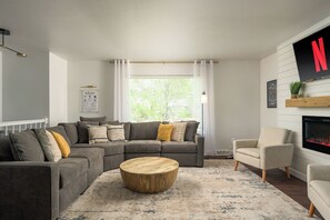 A living room with a sectional sofa, a round coffee table, a fireplace, and a mounted TV.