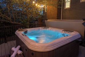 A hot tub on a wooden deck with a brick wall and a tree in the background.