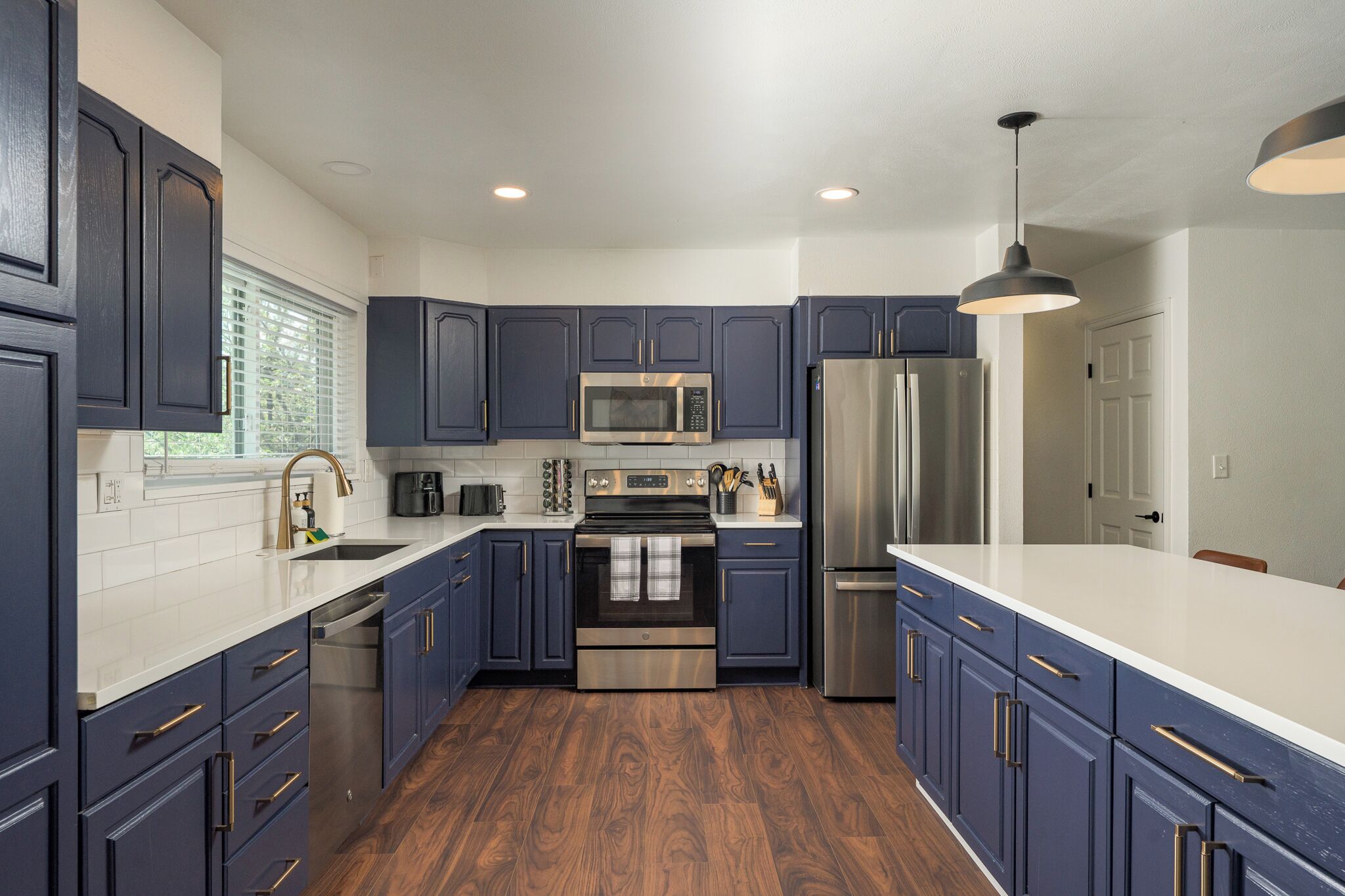 Una cocina moderna con gabinetes azul oscuro, electrodomésticos de acero inoxidable y piso de madera.
