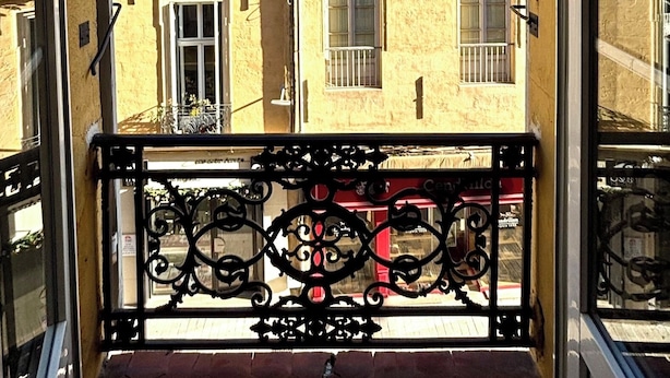 A view of a yellow building with multiple windows and balconies, viewed from a balcony with ornate black metal railings.