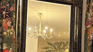 A mirror with an ornate frame, a chandelier, and a floral curtain.