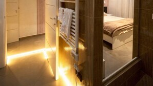 Une chambre d’hôtel moderne dotée d’un dressing, d’un lit recouvert d’une couverture beige et d’un grand miroir qui reflète la pièce.