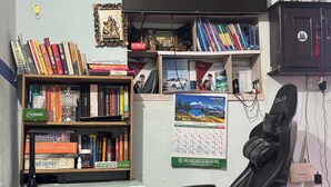 Een kamer met een bureau, een computer, een boekenkast, een agenda en een televisie.