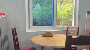 Un coin repas avec une table ronde et quatre chaises en bois dotées de coussins rouges. Une fenêtre offre une vue sur la verdure environnante.
