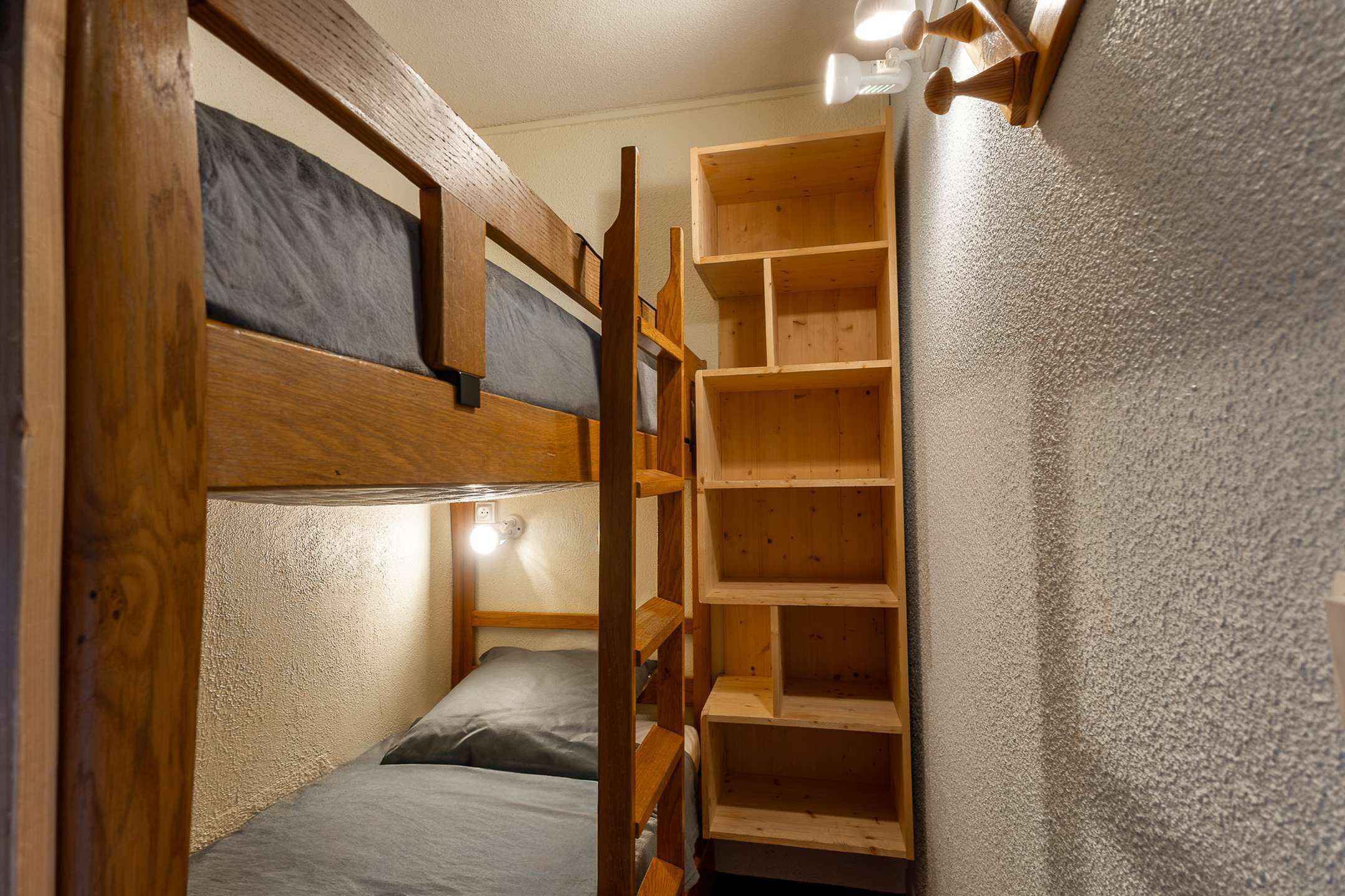 Ein Stockbett mit einer Holzleiter und einer dahingestellt stehenden Regalzeile.