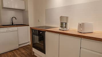 Een koelkast, een oven, een vaatwasser, kookgerei, borden en bestek