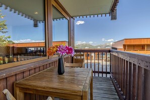 Eine Holzterrasse mit Tisch und Stühlen, eine Vase mit Blumen und Blick auf Gebäude und Berge.