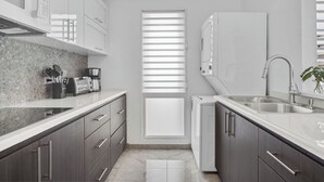 A modern kitchen with dark cabinets, a white countertop, a built-in oven, and a window with blinds. - Designer remodeleded apt.View, Parking, location,NEW listing! (Luquillo)
