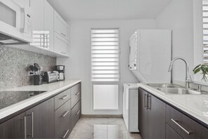 A modern kitchen with dark cabinets, a white countertop, a built-in oven, and a window with blinds. - Designer remodeleded apt.View, Parking, location,NEW listing! (Luquillo)