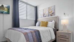 Ein ordentlich eingerichtetes Schlafzimmer mit Bett, Nachttisch und einem Fenster mit Vorhängen.