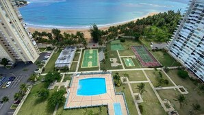 Ein Hochhaus-Hotel mit Swimmingpool, Tennisplätzen und Blick auf den Strand.