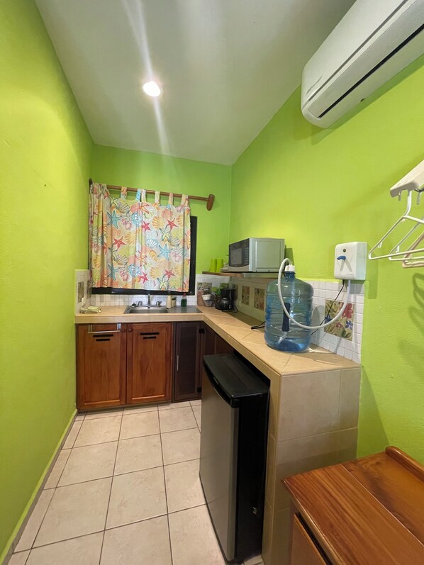 A compact kitchen with green walls, a microwave, a water dispenser, and a dishwasher. - FLORA: Lovely suite in charming Celestun with AC & King bed. (Celestún)