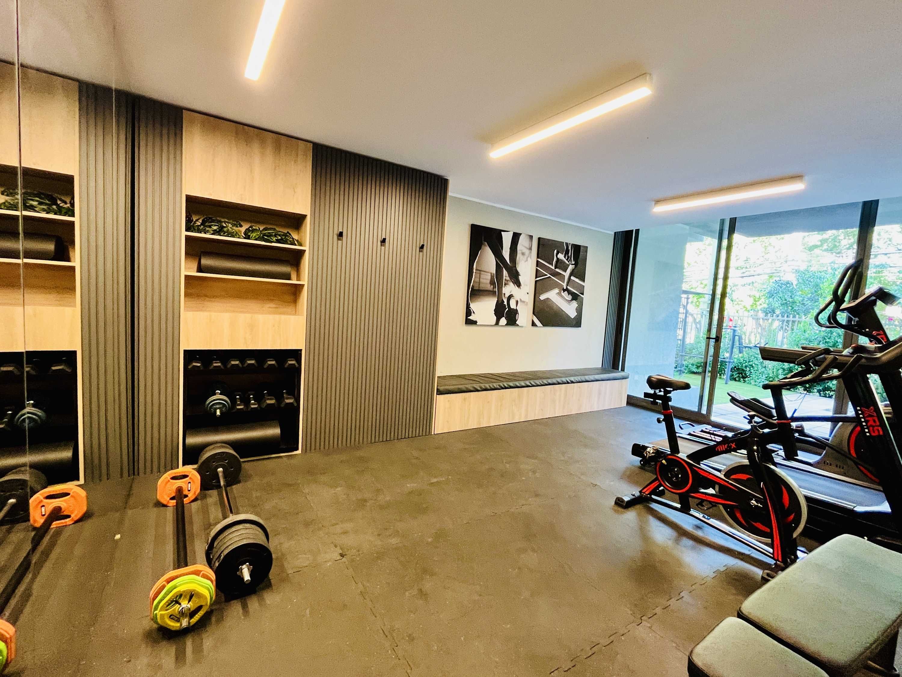 Un gimnasio moderno con equipo de levantamiento de pesas, una bicicleta estática y un amplio ventanal con vistas al exterior.