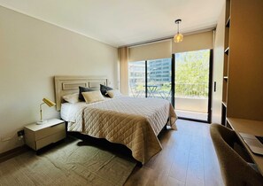 A modern bedroom with a large bed, a bedside table with a lamp, and a view of the outdoors through a sliding glass door. - Studio Las Tranqueras - Fast Wifi, Gym & Laundry (Las Condes)