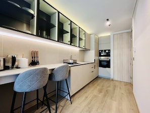 A modern kitchen with a bar area, built-in appliances, and a wooden floor. - Studio Las Tranqueras - Fast Wifi, Gym & Laundry (Las Condes)
