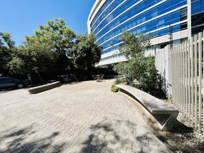 A paved walkway leading to a modern building with a curved facade and a white fence. - Modern Studio Las Tranqueras - Pool, Gym & Laundry (Las Condes)