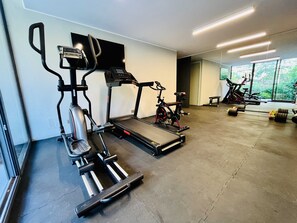 A gym with cardio equipment, a stationary bike, and a weight bench. - Modern Studio Las Tranqueras - Pool, Gym & Laundry (Las Condes)