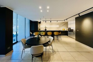 A modern kitchen with a dining area, featuring a round table with chairs, a kitchen island, and a large window providing natural light. - Modern Studio Las Tranqueras - Pool, Gym & Laundry (Las Condes)