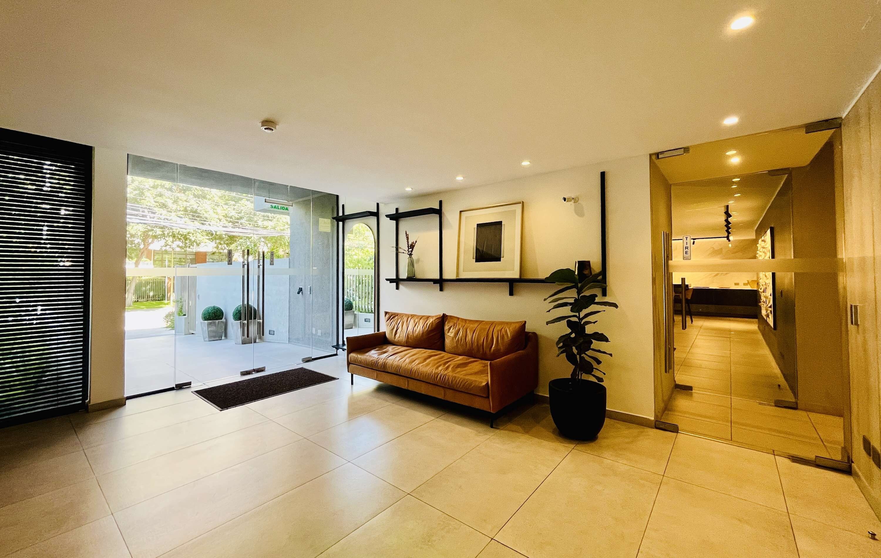 Un intérieur moderne avec un canapé en cuir, une plante en pot et une porte vitrée donnant sur l’extérieur.