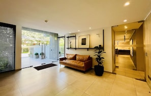 A modern interior with a leather sofa, a potted plant, and a glass door leading outside. - Modern Studio Las Tranqueras - Pool, Gym & Laundry (Las Condes)