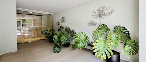 Un interior moderno con un pasillo bordeado de plantas en macetas y un puerta de vidrio que da a un área exterior.