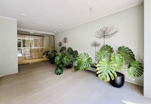 A modern interior with a hallway lined with potted plants and a glass door leading to an outdoor area. - Modern Studio Las Tranqueras - Pool, Gym & Laundry (Las Condes)