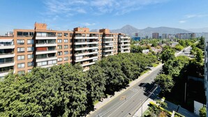 Un edificio residencial de varios pisos con balcones, rodeado de árboles y un cielo despejado.