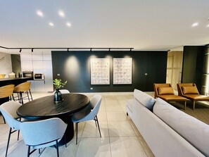 A modern living room with a round dining table, light-colored sofas, and a kitchen in the background. - Modern Studio Las Tranqueras - Pool, Gym & Laundry (Las Condes)