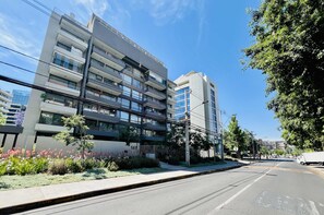 A multi-story building with balconies, a clear sky, and a street with vehicles. - Modern Studio Las Tranqueras - Pool, Gym & Laundry (Las Condes)