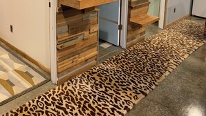 Een hal met een houten wanddecoratie, een tapijt met luipaardprint en een deur met een ruitpaneel.