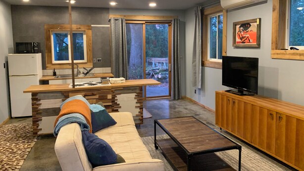 Een moderne woonkamer met een bank, televisie, houten kast en een keukenhoek met een koelkast en magnetron.