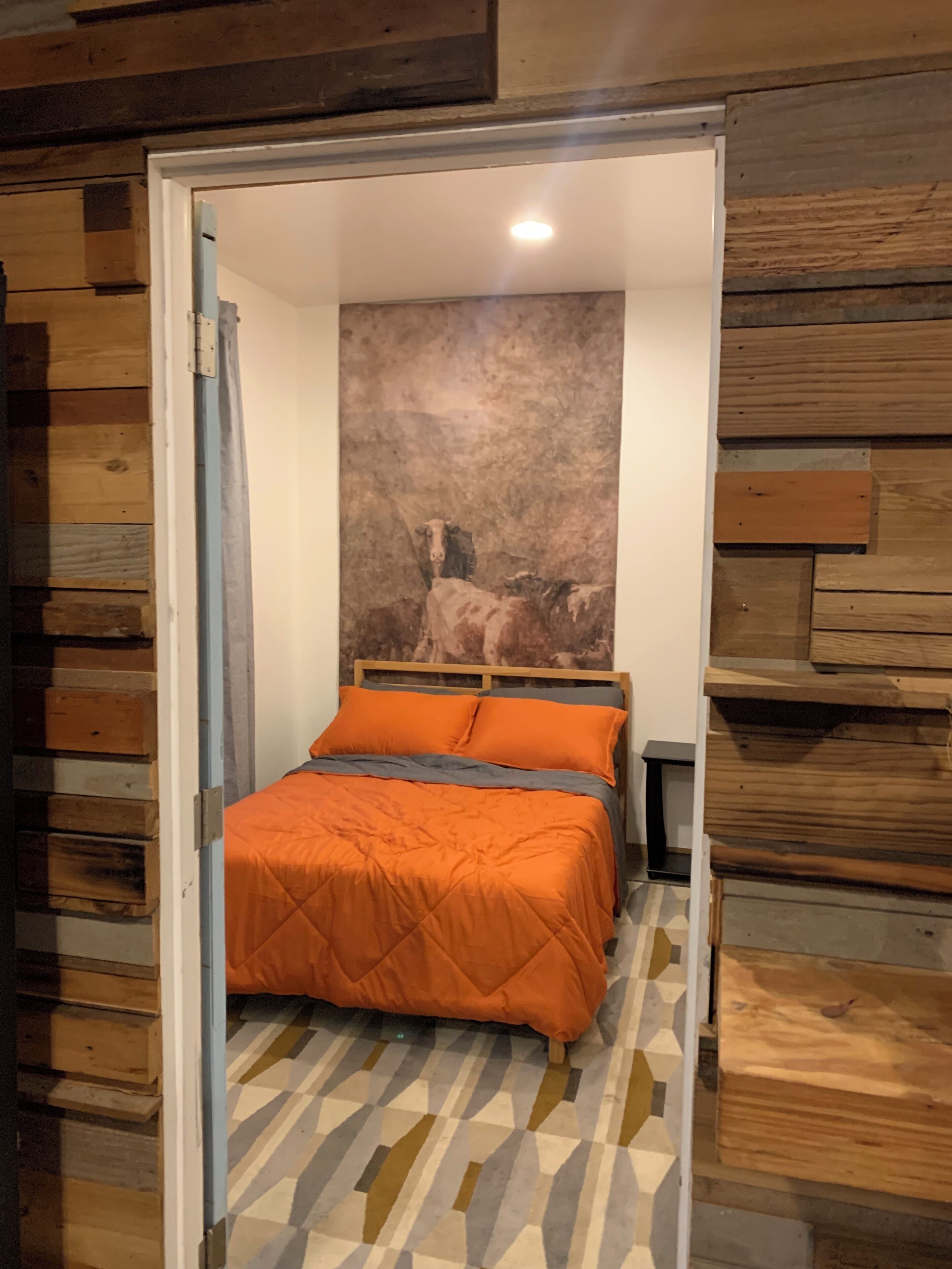 Une chambre avec un mur revêtu de panneaux en bois, un lit avec une literie orange et un sol à motifs géométriques.