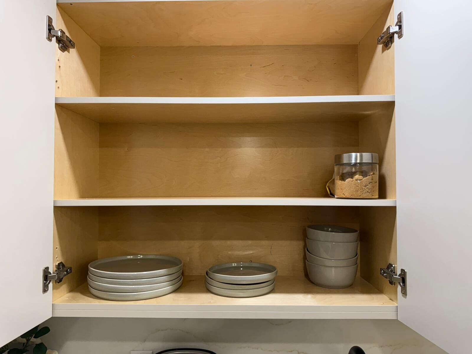 A kitchen cabinet with three shelves, each containing kitchenware.