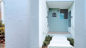 En smal gång som leder till en byggnadsentré, med en skylt med siffran ’20’, en trälogo och en ventilationsöppning på väggen.