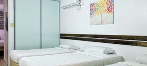 Una habitación con dos camas, cabecero de madera, aire acondicionado de pared y un cuadro abstracto de colores.
