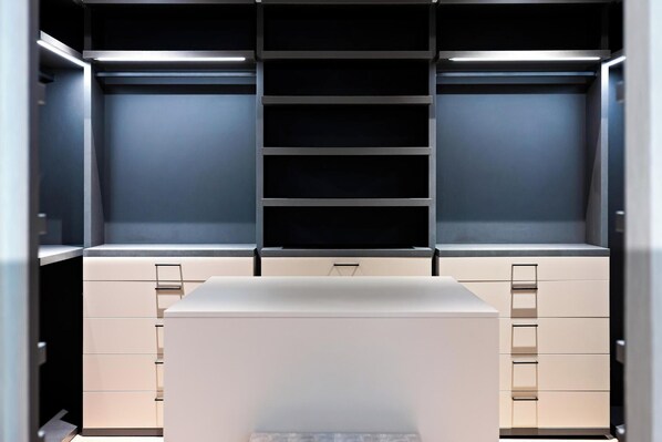 A modern, well-lit walk-in closet with multiple shelves and drawers, featuring a minimalist design and neutral color palette.